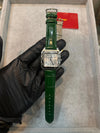 Luxury men’s watch with green leather strap and square silver case, showcased on gloved hand.