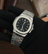 Luxury stainless steel men's watch with black dial held by gloved hand, modern design
