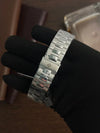 Luxury stainless steel men’s watch bracelet with clasp, held by gloved hand, on wood background