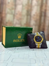Luxury men's Rolex two-tone watch with black dial beside green branded box on table