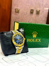 Luxury men's gold and silver wristwatch with blue dial, displayed beside green Rolex box.