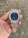 Luxury men’s silver wristwatch with blue dial and metal band, held in hand outdoors, premium accessory.