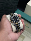 Luxury men's two-tone Rolex Submariner watch with black dial and gold bezel held in hand